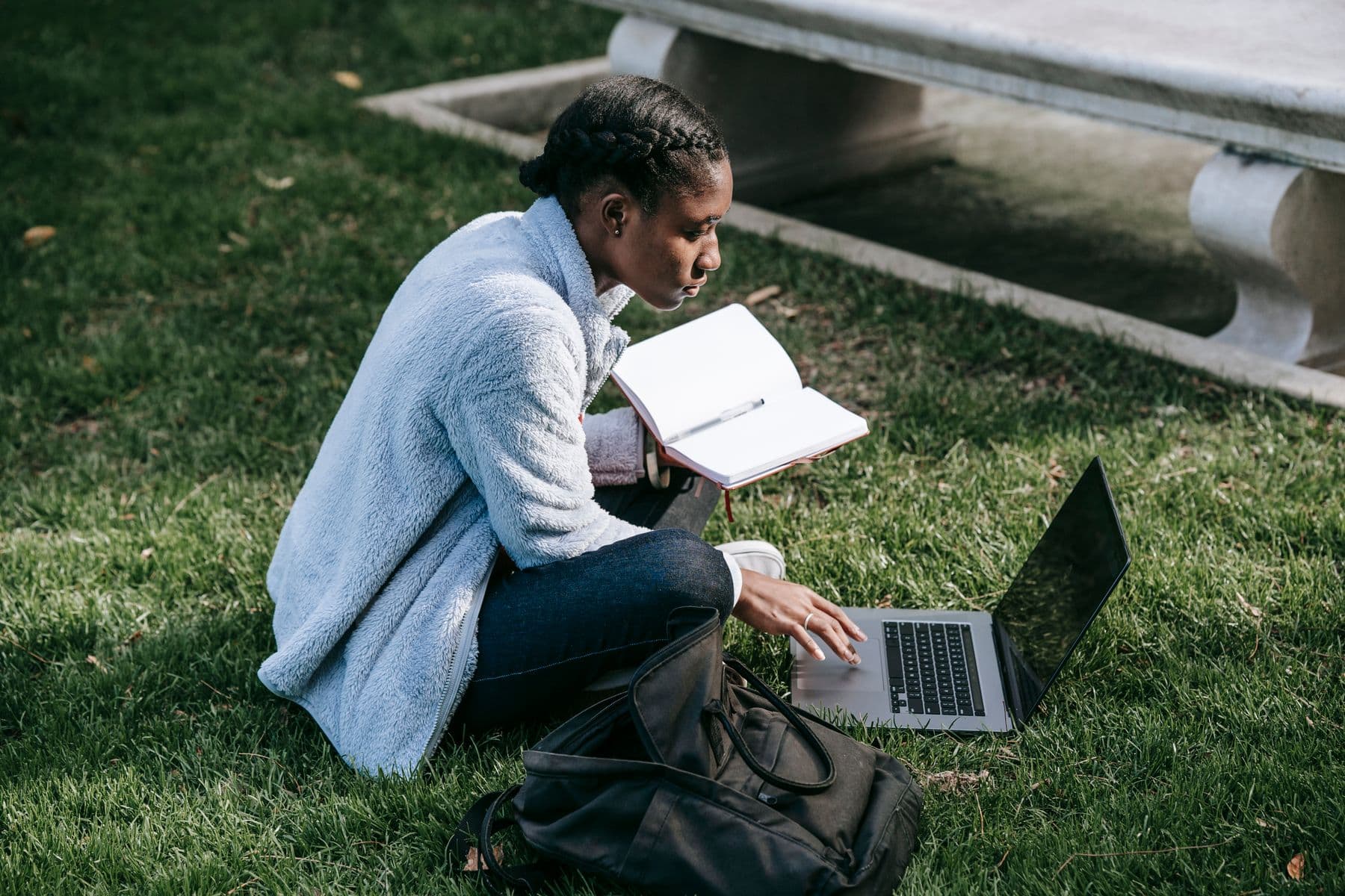 A student planning with a notebook and laptop outdoors